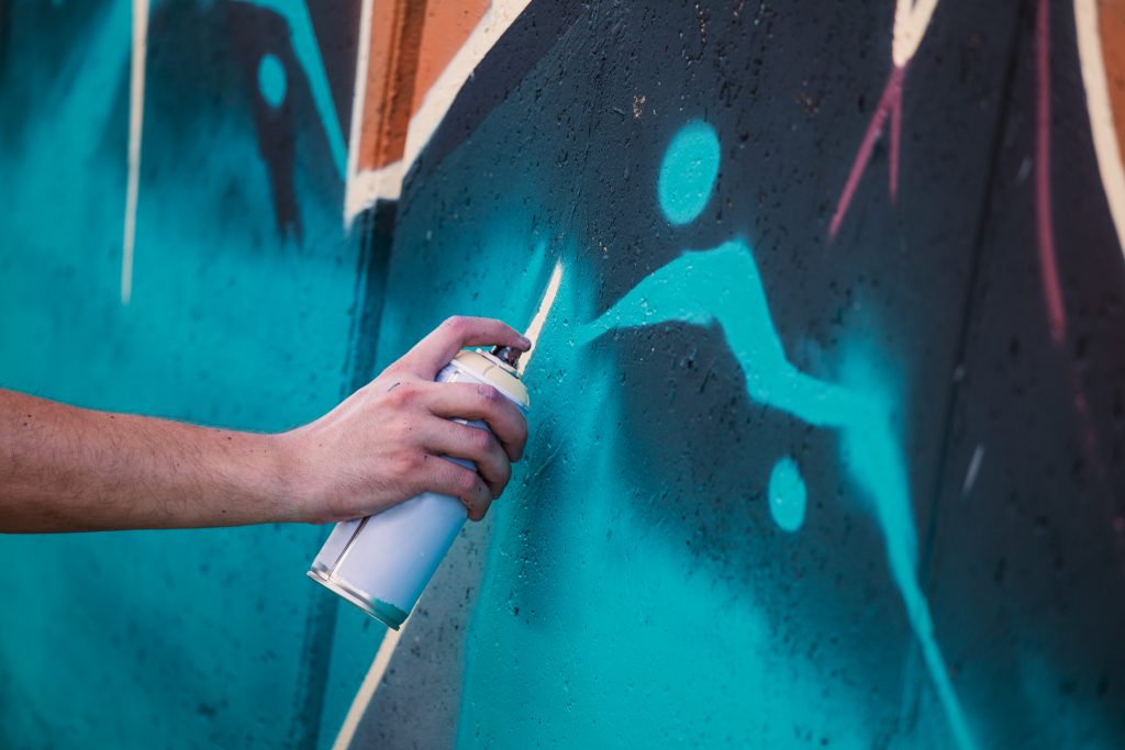 Street artist painting colorful graffiti on generic wall - Modern art concept with urban guy performing and preparing live murales with multi color aerosol spray