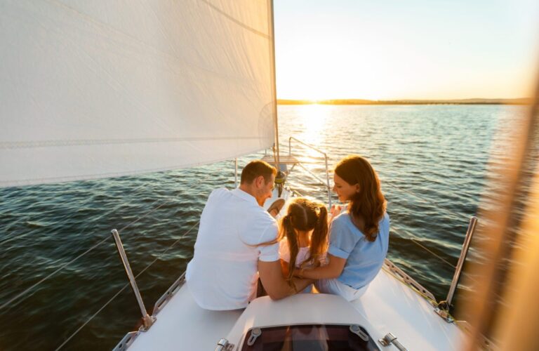 Family Yacht Sailing. Parents And Little Daughter Sitting Together On Sailboat Deck Hugging Enjoying Sea Trip. Back View, Free Space